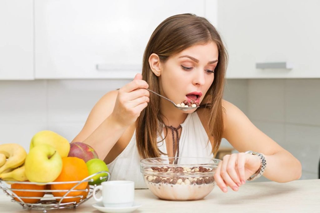 Foto de mulher sentada em uma mesa comendo rápido e olhando para o relógio, refeições