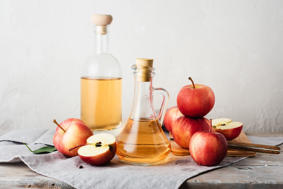 Foto de vidros com vinagre de maçã, rodeados com fatias e frutas inteiras - Metrópoles