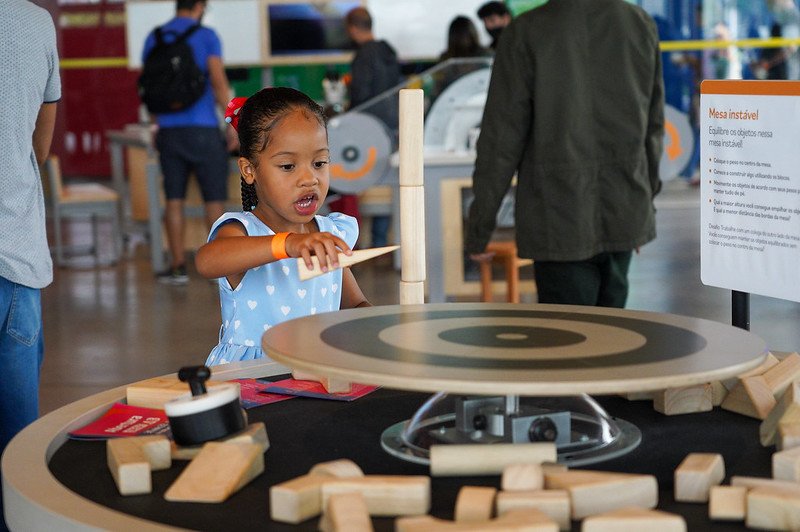 Fotografia colorida de uma garota brincando em uma mesa de madeira