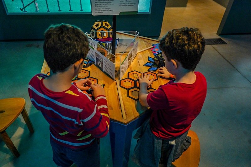 fotografia colorida de dois meninos brincando com brinquedos em uma mesa de madeira