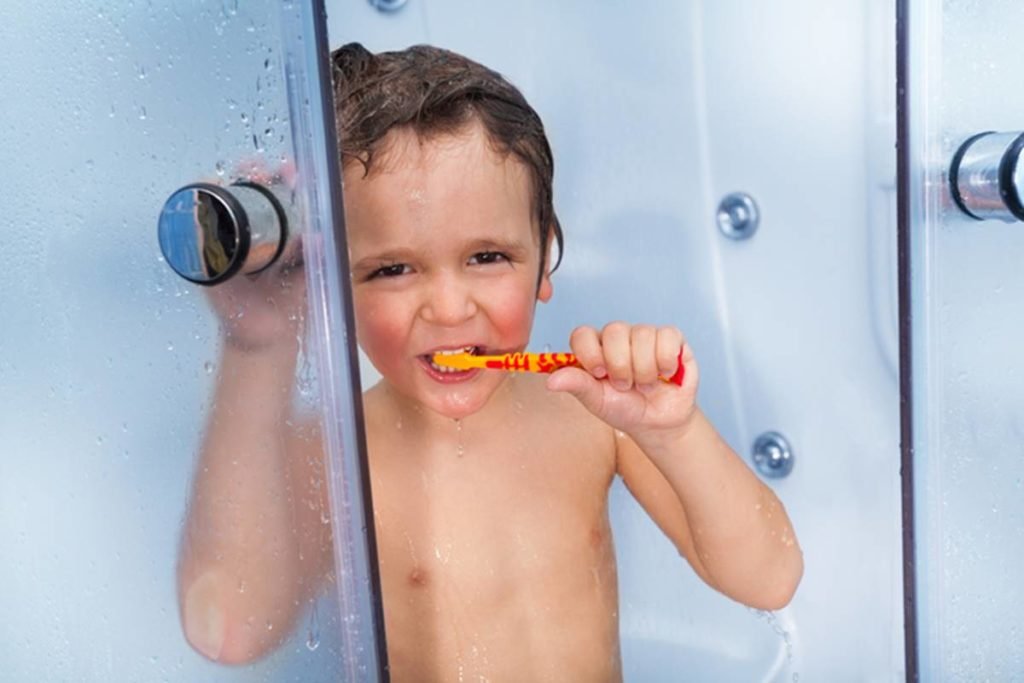 Imagem colorida de criança esconvando os dentes enquanto toma banho