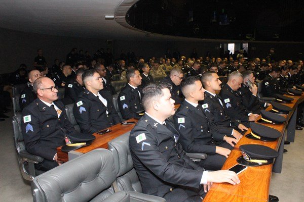 Fotografia colorida mostra oficiais sentados em plenário