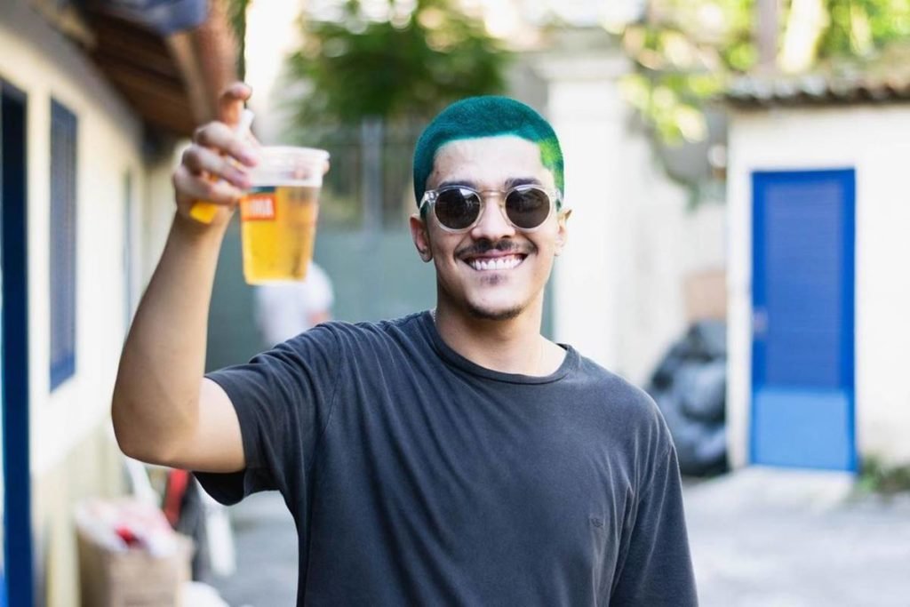 Foto colorida de Chico Veiga com o cbaelo verde e copo de cerveja - Metrópoles