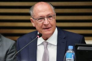 Geraldo Alckmin sentado, de óculos e terno, fala ao microfone - Metrópoles
