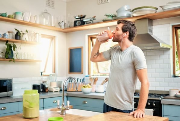 Jovem ingere shake de proteína na cozinha de uma casa