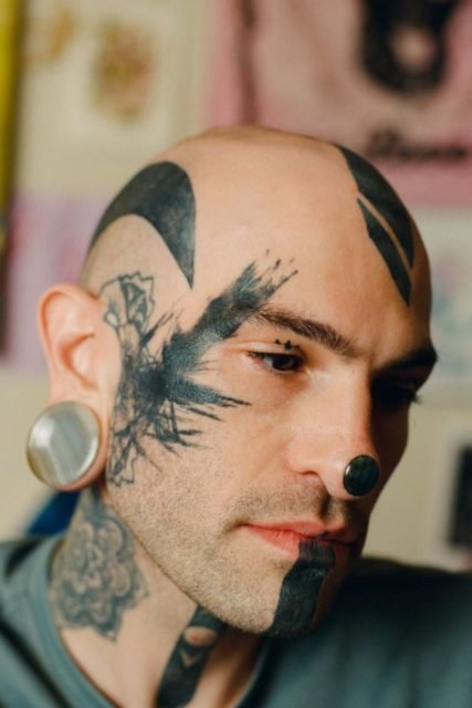 Na foto, homem aparece de frente com o rosto tatuado de preto - Metrópoles