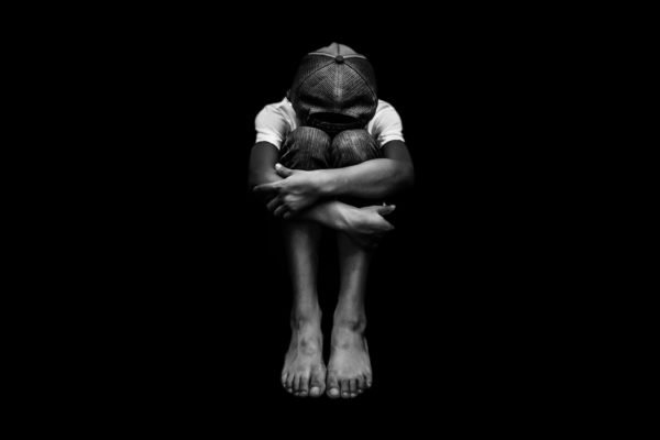 Foto preto e branco de criança descalça com rosto escondido - Metrópoles