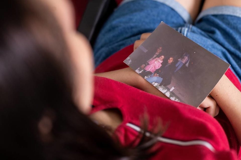 Foto colorida de uma mulher branca com camiseta vermelha e shorts jeans olhanto uma foto - Metrópoles