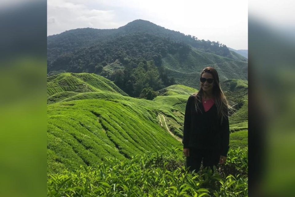 Mulher com casaco vermelha em meio a um campo verde - Metrópoles