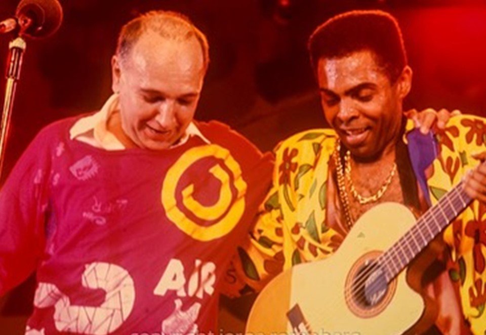 João Donato (de vermelho) e Gilberto Gil (amarelo com estampa) abraçados em foto histórica e não datada