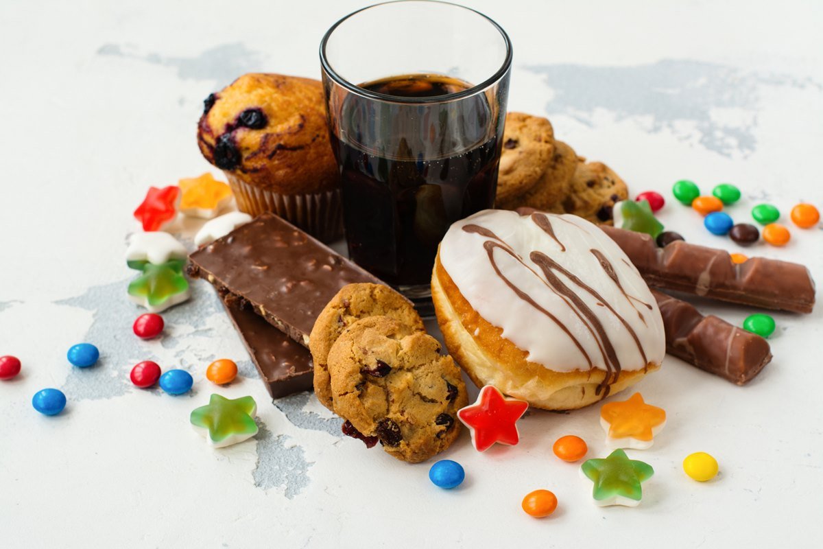 Foto colorida de alimentos ultraprocessados, incluindo balinhas, barras de chocolate, copo de refrigerante, donuts, cookies e muffins - Metrópoles