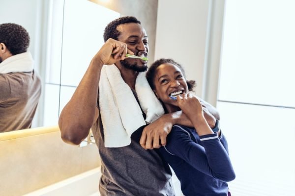 Foto mostra um homem e uma adolescente em um banheiro. Eles escovam os dentes juntos - Metrópoles