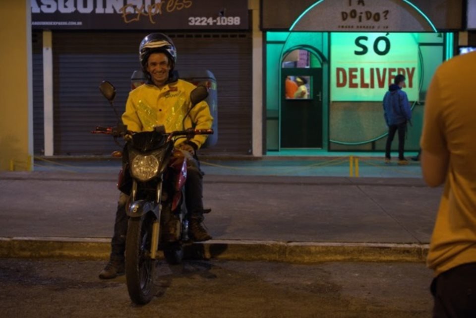 Foto do Documentário brasiliense Da Porta Pra Fora.. Motoboy com roupa amarela no meio da rua - Metrópoles