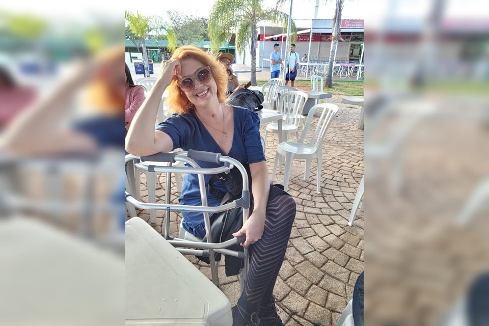 mulher sentada com andador vestida com blusa de cor escura e de calça