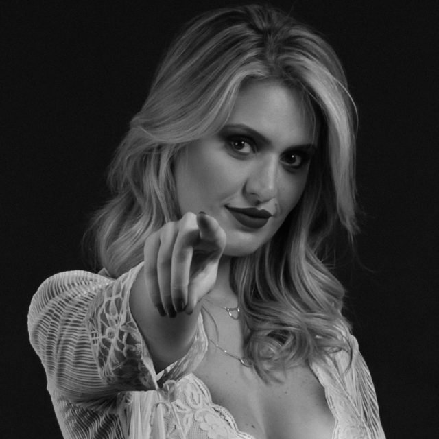 Foto preta e branca de Karen Bacic. Ela aponta o dedo para a câmera - Metrópoles