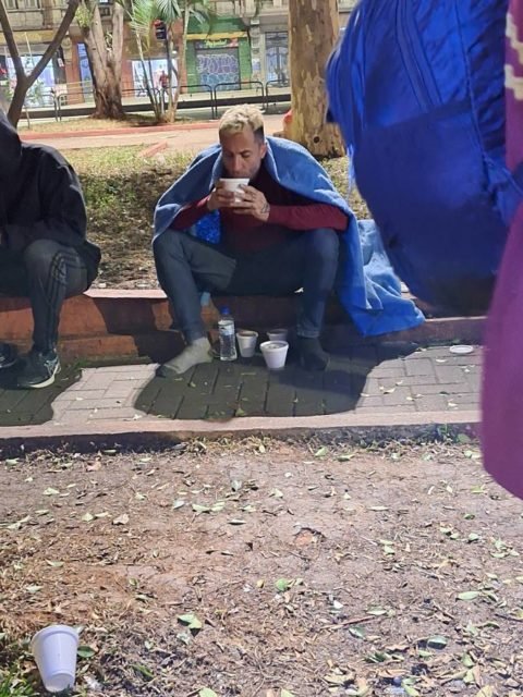 Imagem mostra homem sentado na Praça Marechal Deodoro, com coberta azul, tomando sopa - Metrópoles