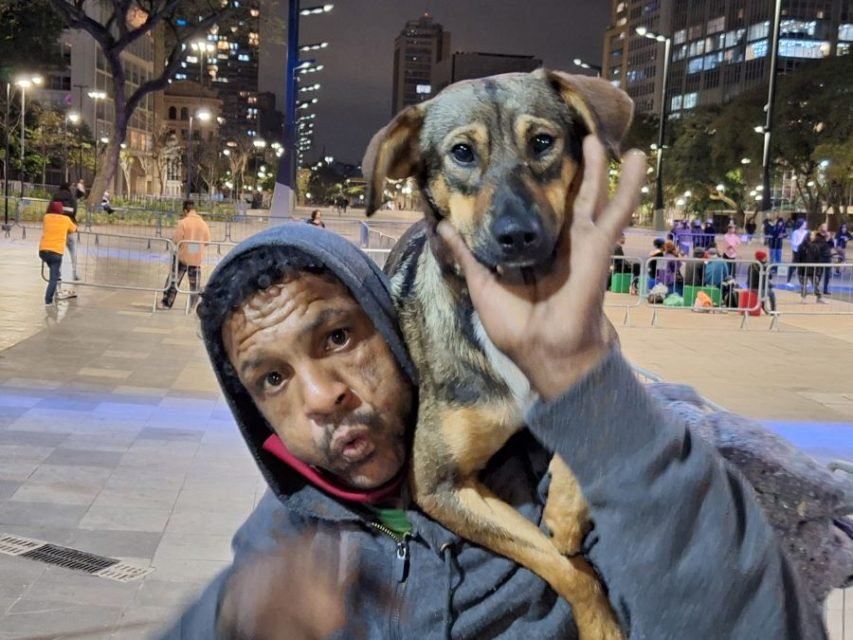 Imagem mostra homem com as bochechas estufadas, segurando cachorro sobre o ombro - Metrópoles