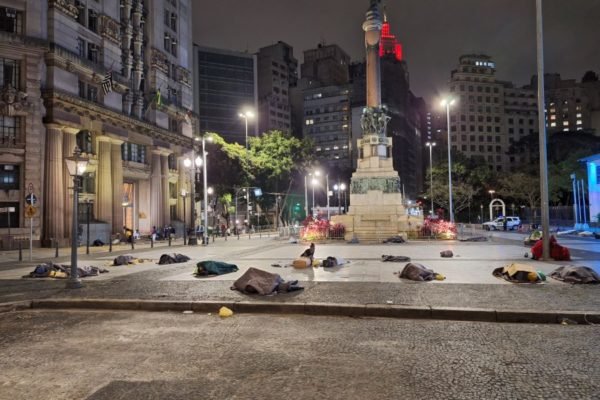 Imagem mostra pessoas dormindo no chão em frente a monumento - Metrópoles