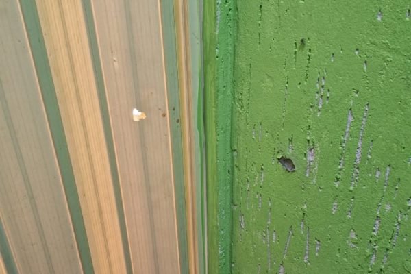 Buraco em porta sanfonada bege e parede verde provocada por tiro