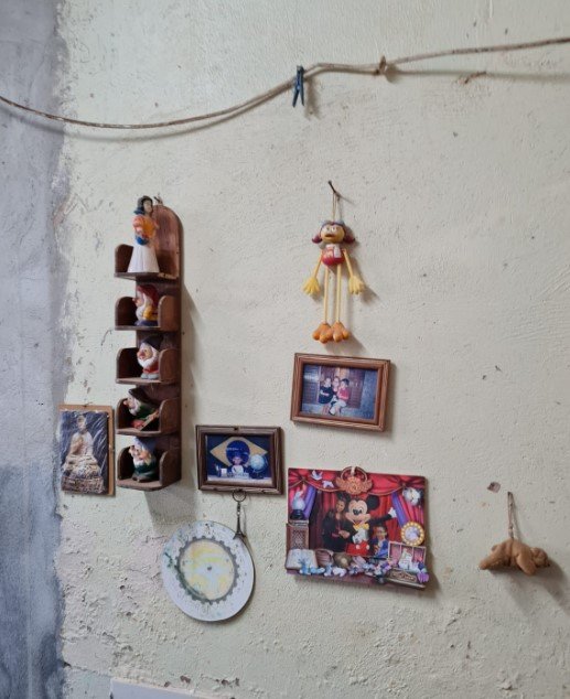 Parede bege com diversos objetos pendurados, como fotos e bonecos