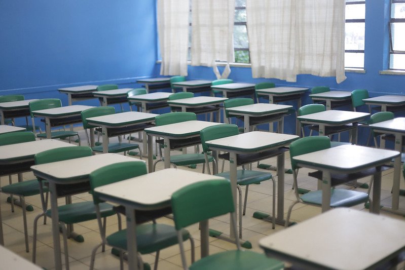 Imagem colorida mostra sala de aula vazia em SP. Local tem quatro fileiras com mesas brancas e cadeiras verdes - Metrópoles