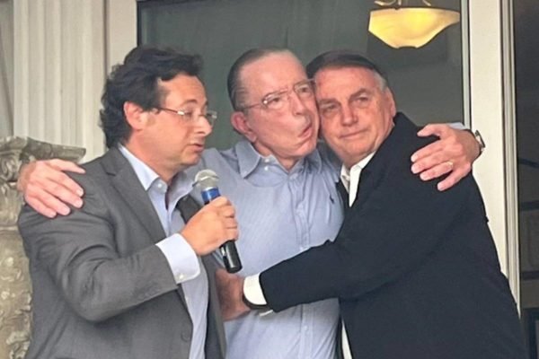 imagem colorida mostra três homens abraçados, um segura um microfone: fabio wajngarten, doutor Antonio Macedo e jair bolsonaro
