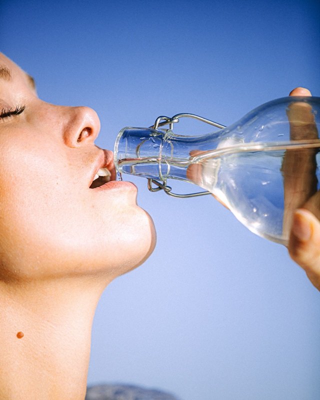 Rosto de mulher jovem ingerindo água de garrafa de vidro - Metrópoles