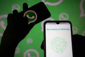 foto colorida com silhueta de mão segurando celular com logo do whatsapp e outra mão segurando a tela de bem-vindo ao whatsapp - metrópolea