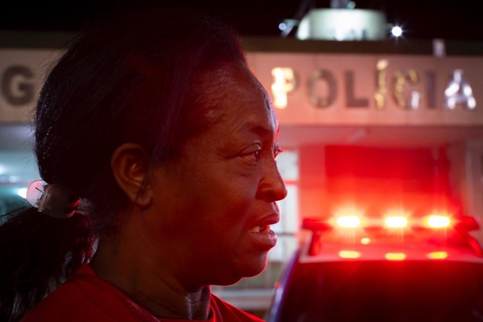 Imagem de mulher negra olhando para o lado usando camiseta vermelha em frente a delegacia - Metrópoles