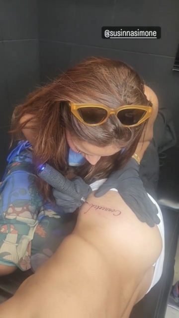 Foto colorida de Anitta. A cantora está fazendo uma tatuagem em Simone Susinna - Metrópoles