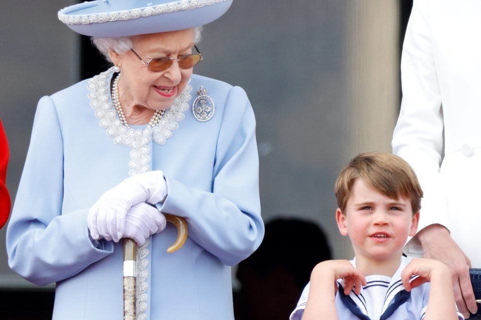 Foto colorida. Imagem mostra a falecida rainha Elizabeth II, uma idosa branca com conjunto de roupa e chapéu lilás ao lado do bisneto, Louis. O garotinho tem cinco anos e tem cabelos loiros e lisos - Metrópoles