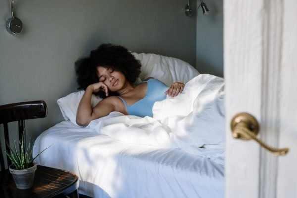 Jovem mulher negra dormindo deitada em cama - Metrópoles