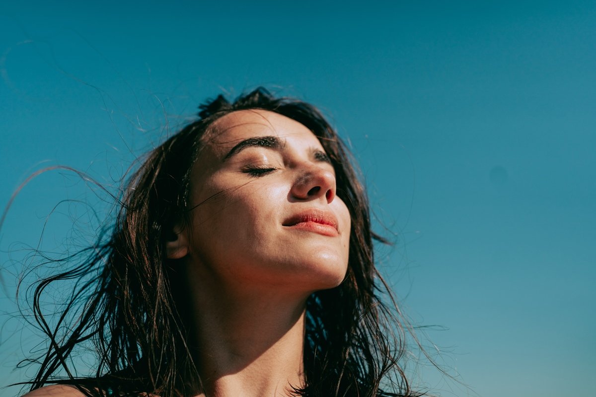 Foto colorida. Mulher branca com cabelos pretos está tomando sol - Metrópoles