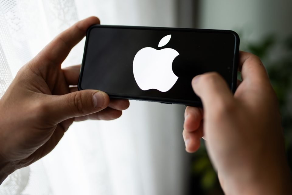 Foto colorida. Uma mão está segurando um celular. A tela está preta com a logo da Apple na cor branca - Metrópoles