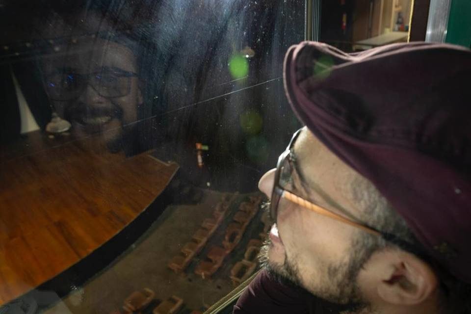 homem sorrindo com reflexo em uma vidraça ao ver palco de teatro iluminado
