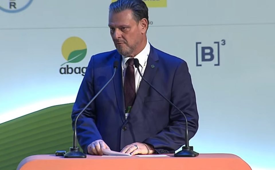 Imagem colorida do ministro da Agricultura, Carlos Fávaro, vestindo um terno azul escuro, com gravata escura, falando ao microfone em um evento do agronegócio - Metrópoles