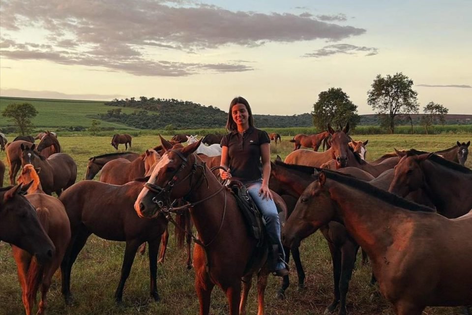 mulher jovem montada em cavalo com cavalos ao redor - metrópoles