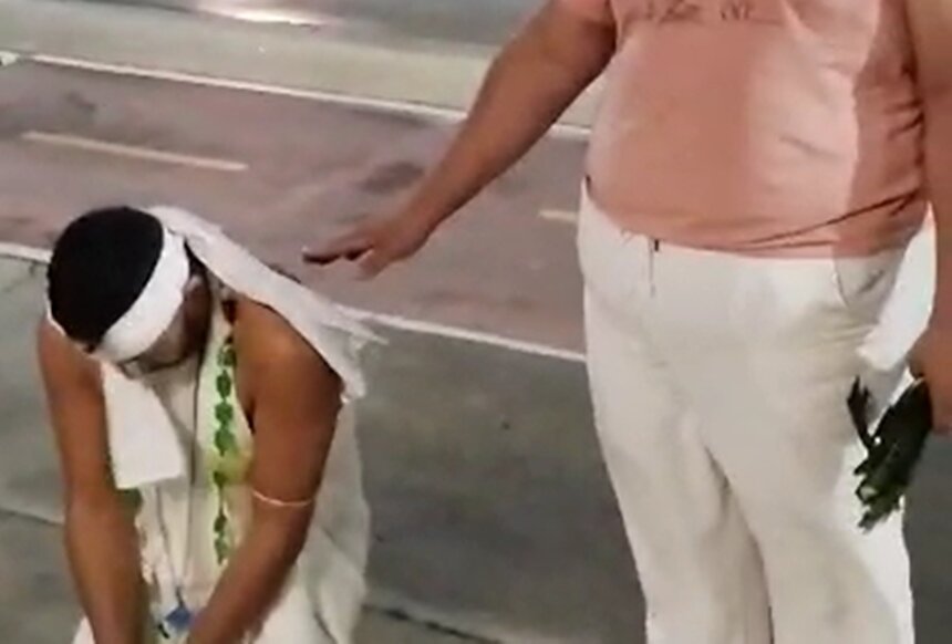 Em foto colorida homem com roupa branca de religião de matriz afro está ajoelhado em calçada - Metrópoles