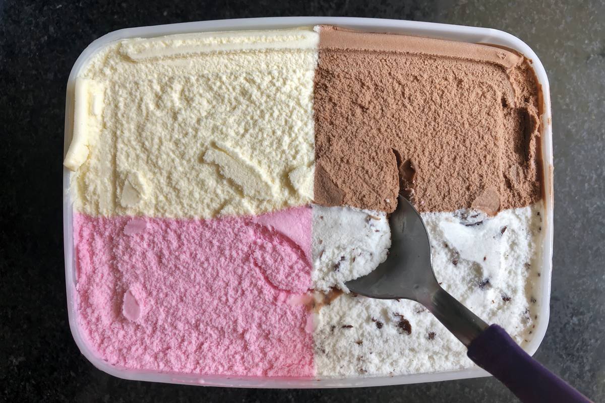 Foto colorida de pote de sorvete. São quatro sabores. Um colher está dentro do alimento - Metrópoles