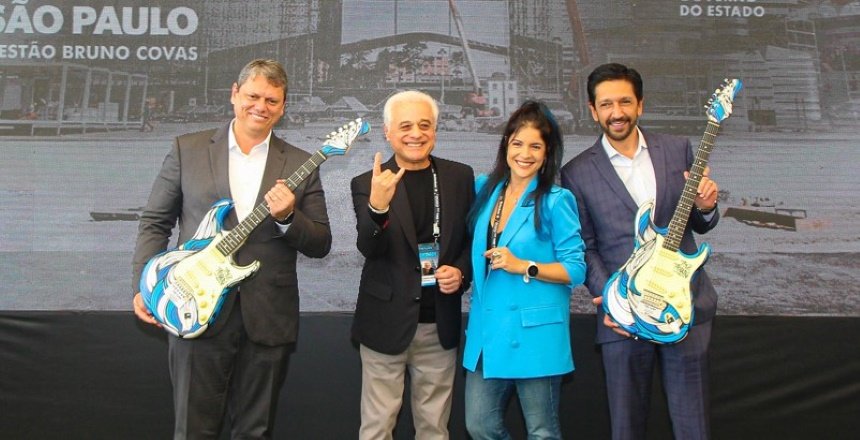 Foto colorida - Governador Tarcísio (esq.) e Ricardo Nunes (dir.) entre os organizadores do festival The Town; Tarcísio e Nunes seguram guitarras azuis
