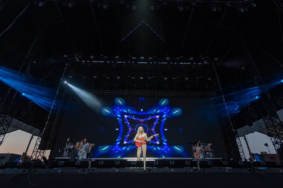 Foto do show de Giulia Be, realizado em Portugal. A cantora é branca, loira, está com vestido claro e toca uma guitarra - Metrópoles