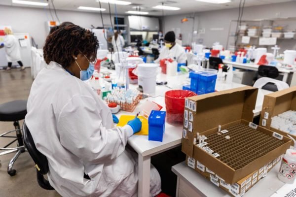 imagem colorida mostra pessoas com jaleco branco e máscara em laboratório com testes laboratoriais e materiais de testagem - Metrópoles