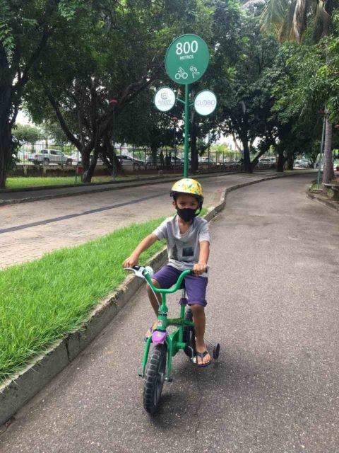 Foto mostra Bernardo, menino com hemofilia, andando de bicicleta em um parque - Metrópoles