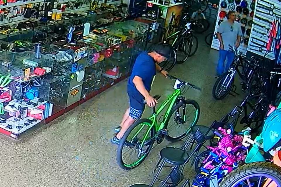 Homem de roupa azul e boné escolhendo uma bicicleta verde