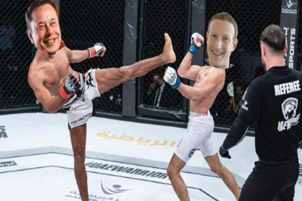 Imagem de um meme que mostra os bilionários Elon Musk e Mark Zuckerberg lutando em um octógono. Eles estão sem camisa e de bermuda branca, observados por um árbitro que veste roupa preta. Musk tenta acertar um chute de pé esquerdo em Zuckerberg - Metrópoles