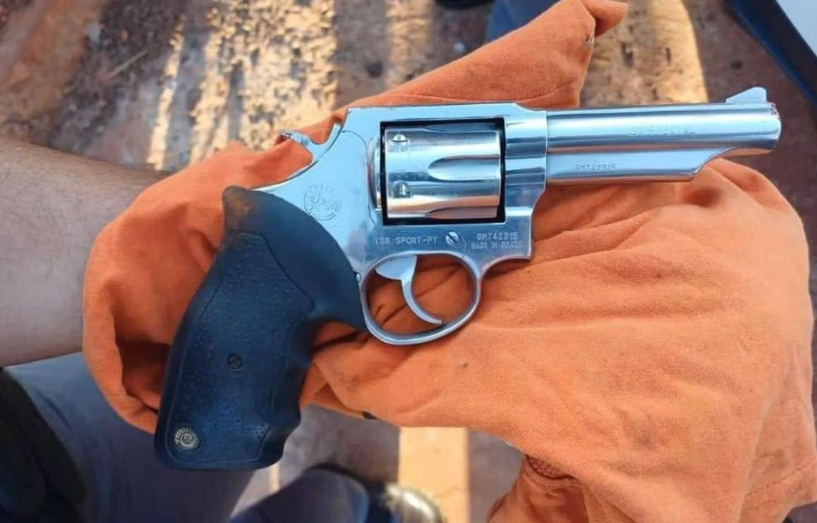 Imagem colorida mostra um revólver calibre 38 prateado com o cabo preto envolvido em um pano laranja - Metrópoles