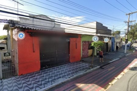 Foto colorida mostra estabelecimento com fachada vermelha e portão preto. O dia é ensolarado - Metrópoles