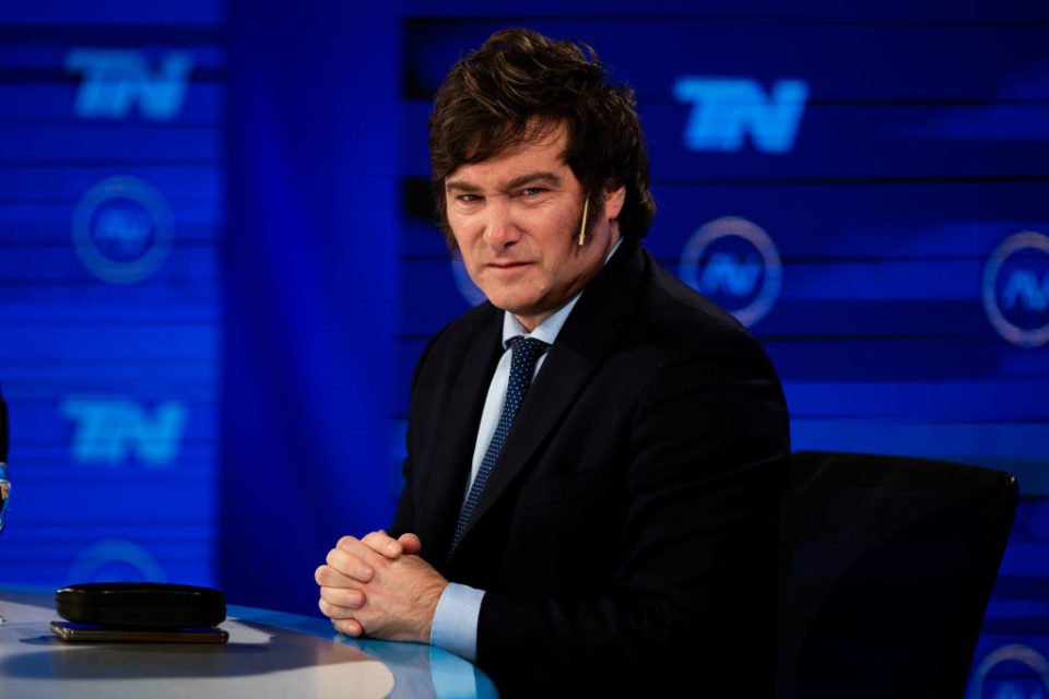 Javier Milei sentado em programa de televisão, com fundo azul - Metrópoles