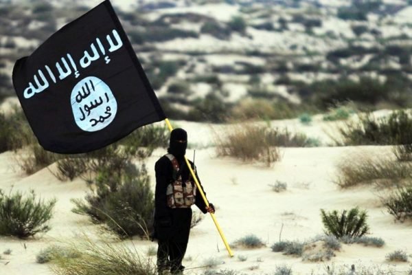 Imagem colorida mostra membro do Estado Islâmico segurando a bandeira do grupo terrorista - Metrópoles