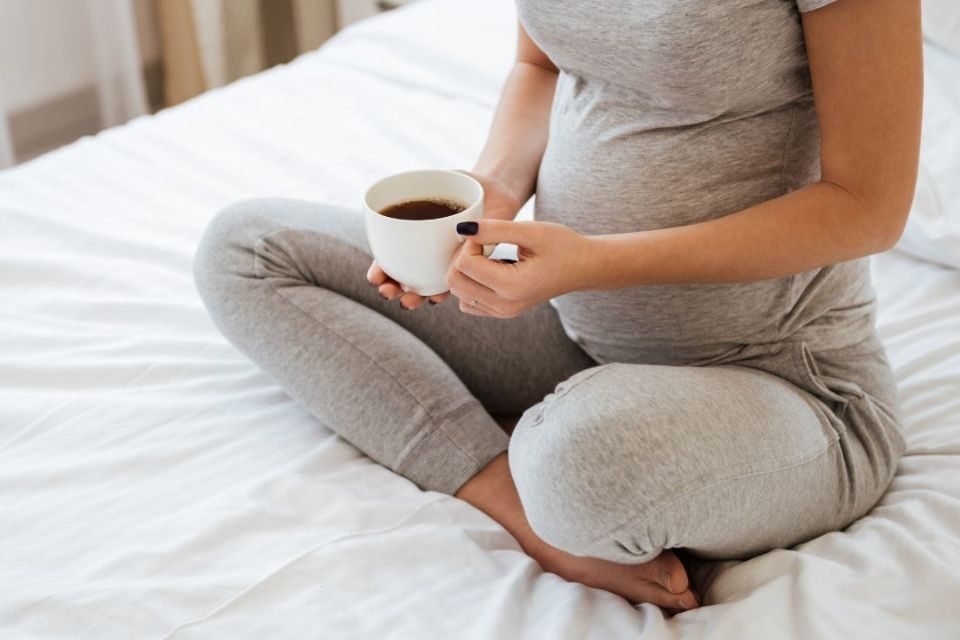 Mulher gravida sentada na cama tomando café - Metrópoles